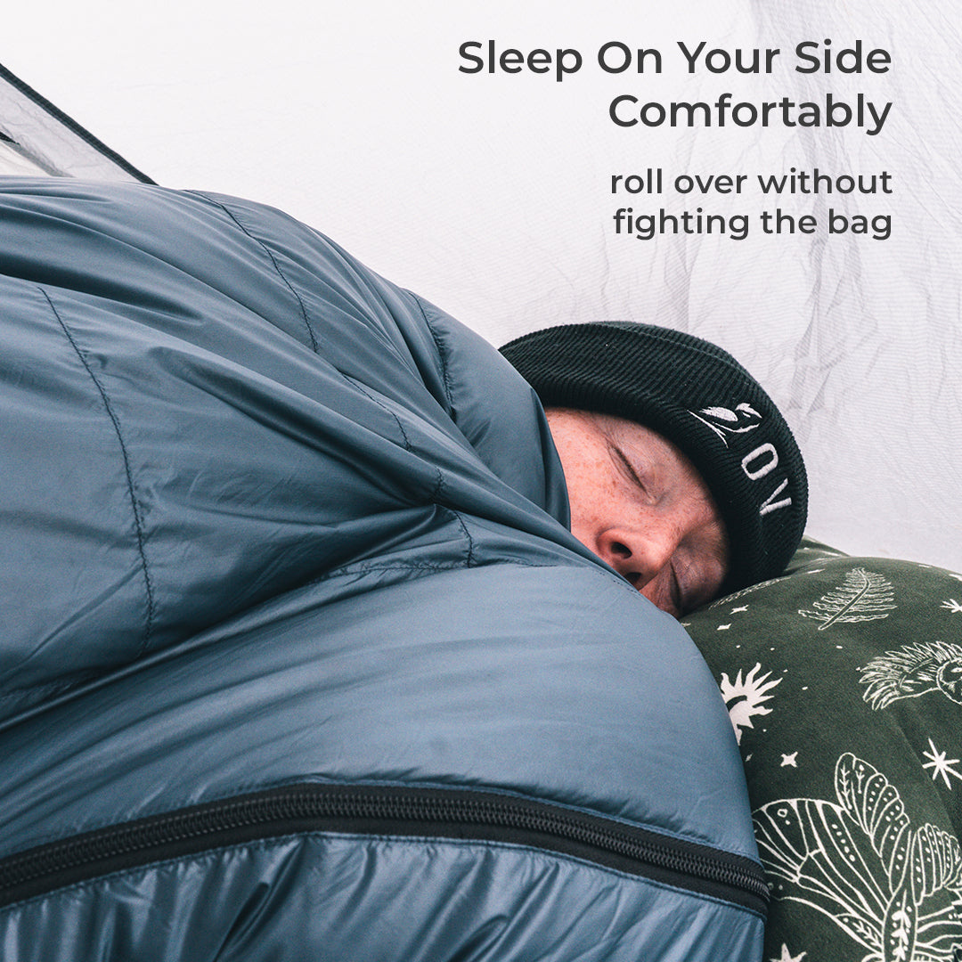 A person sleeping comfortably inside a blue sleeping bag, rolled over to show the side zipper.