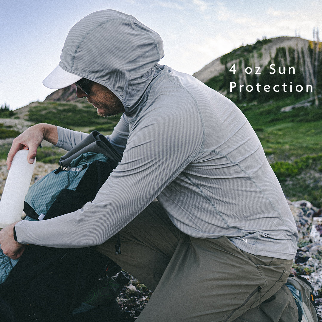 Gray - man on mountain top wearing sun shirt and adjusting gear in backpack