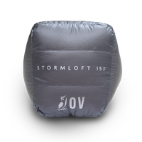 Bottom view of the blue Outdoor Vitals StormLoft 15F topquilt packed inside its compression stuff sack, displaying the printed product name and OV owl logo.