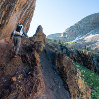 rear view of man wearing ultralight backpack for thru-hiking while climbing steep incline