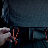 Close-up view showing a hand adjusting the bottom attachment point with elastic cord locks on the Outdoor Vitals Skyline 30 Fastpack, designed for securing gear like trekking poles or sleeping pads.