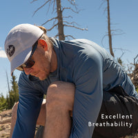 Blue - A man outdoors wearing a blue long-sleeve sun shirt, crouching in a natural setting 