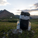 Outdoor Vitals CS40 Ultra Backpack fully packed with water bottles in the side pockets and gear strapped to the top, resting on a grassy alpine ridge with mountains in the background.