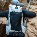 Back view of a hiker navigating a narrow canyon carrying the Outdoor Vitals CS40 Ultra Backpack, featuring top Y-strap gear attachment, dual side water bottle pockets, and bottom lash points.