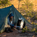A bearded camper resting inside a trekking-pole tent while preparing food next to the Outdoor Vitals CS40 Ultra Backpack at a backcountry campsite in a canyon landscape.