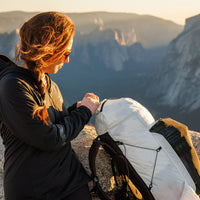 Woman in a hooded jacket adjusting her CS40 Ultra backpack on a rocky summit