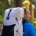 Close-up profile of a hiker wearing the Outdoor Vitals CS40 Ultra Backpack, highlighting the top compression strap, owl logo badge, side cords, and stretch mesh pocket on a forest trail.