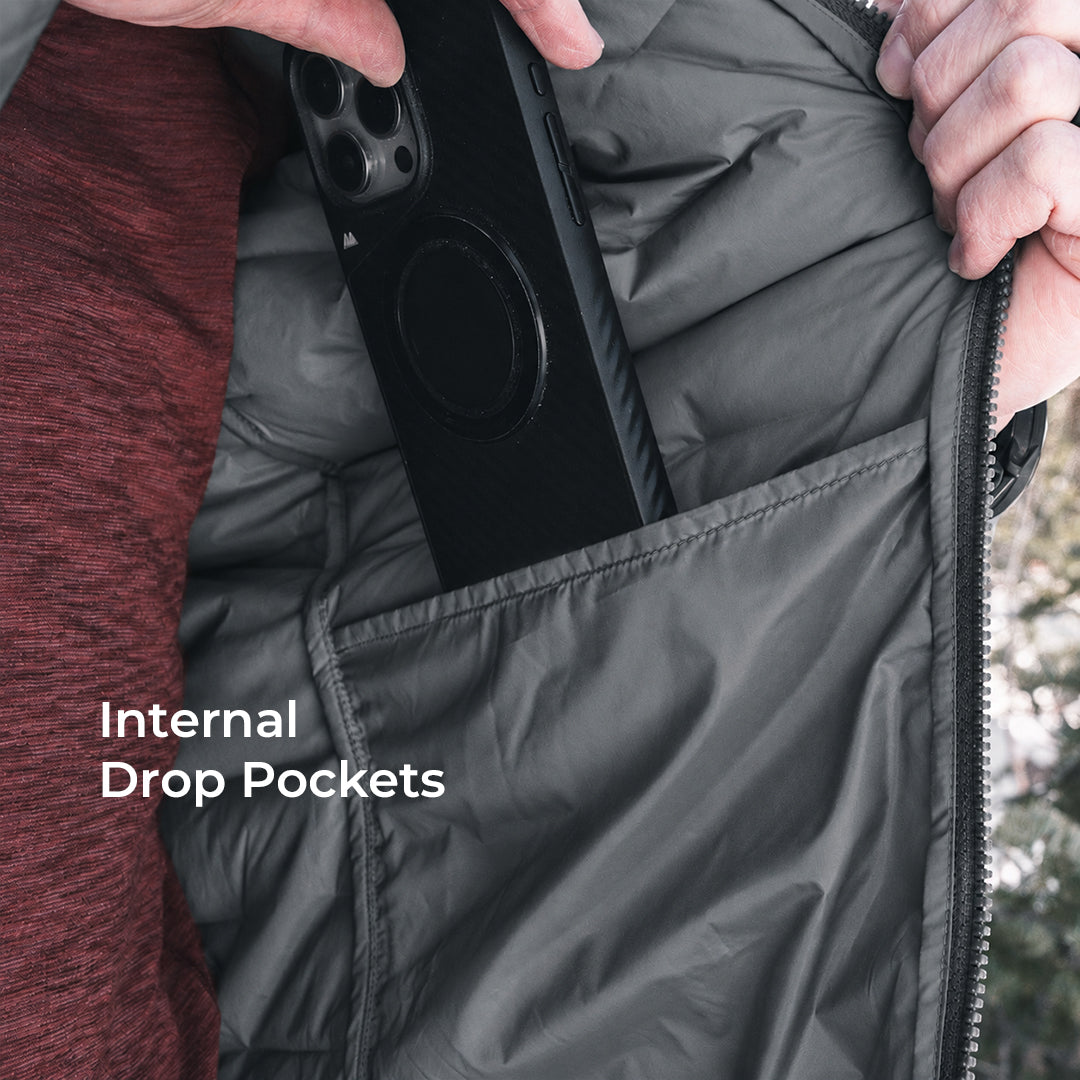Close-up of a person opening a dark gray puffer jacket to show an internal drop pocket holding a black smartphone. White text on the image reads 'Internal Drop Pockets'.