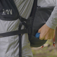 Hiker reaching into the bottom pocket of the Outdoor Vitals Skyline 30 Fastpack while wearing it.