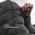 Close-up of a person adjusting the drawstring hood of a dark gray puffer jacket, with white text overlay reading '2-Way Adjustable Hood'.
