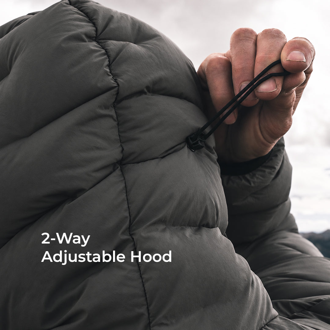 Close-up of a person adjusting the drawstring hood of a dark gray puffer jacket, with white text overlay reading '2-Way Adjustable Hood'.