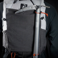 Close-up rear view of the Outdoor Vitals Skyline 30 Fastpack demonstrating an ice axe securely attached using the pack's dedicated side attachment loops and shock cord retainers.
