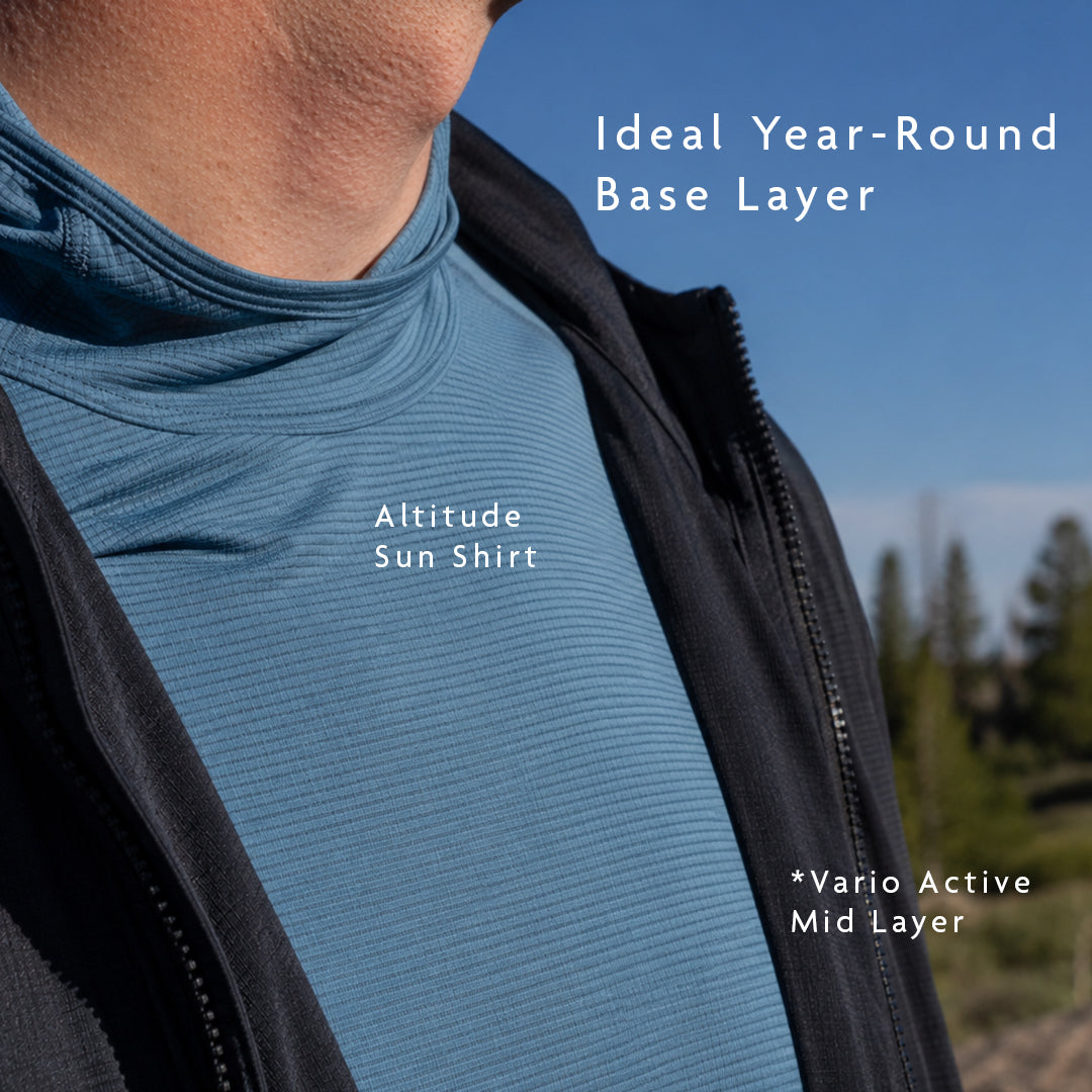 Blue - Close-up of a person outdoors wearing a blue sun shirt under a black zip jacket, with overlaid text reading 'Ideal Year-Round Base Layer'