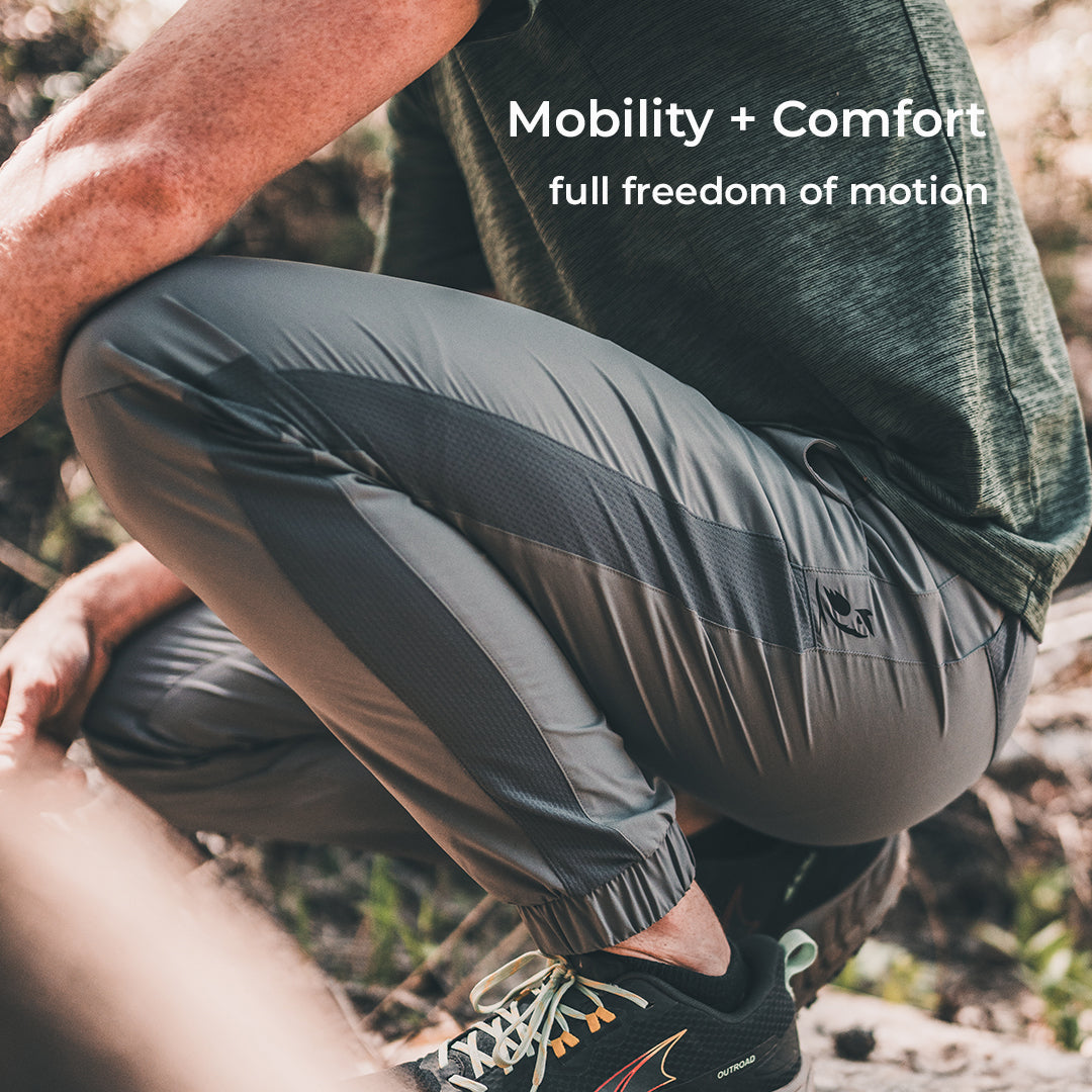 A person wearing gray joggers is crouching in a wooded area. "Mobility + Comfort, full freedom of motion" is overlaid in the top right.