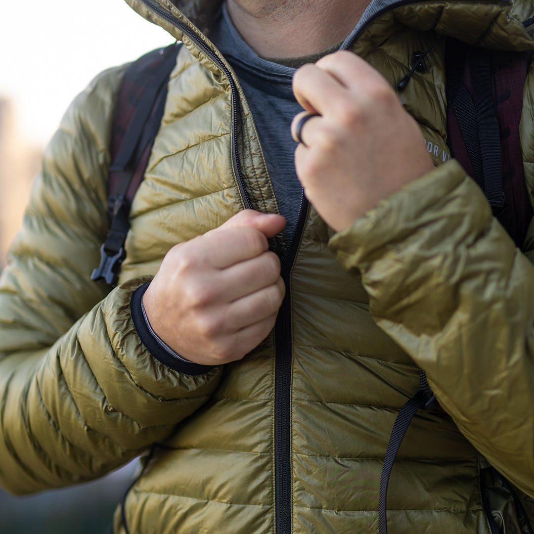 Close-up of a person zipping up a NovaUL down jacket while wearing a backpack.