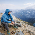 Hiker wearing the Outdoor Vitals Vario Jacket with the hood up on a rocky mountain overlook