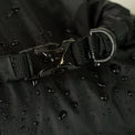 Extreme close-up of a water-resistant roll-top dry sack buckle closure with an attached D-ring, featuring water droplets on the durable coated fabric surface.
