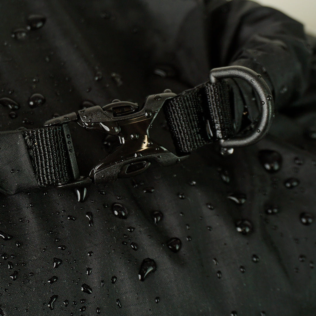 Extreme close-up of a water-resistant roll-top dry sack buckle closure with an attached D-ring, featuring water droplets on the durable coated fabric surface.