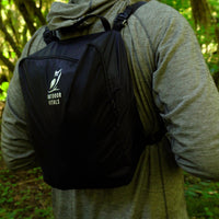 Rear view of a hiker wearing an Outdoor Vitals modular accessory pack secured to shoulder straps on an outdoor trail.