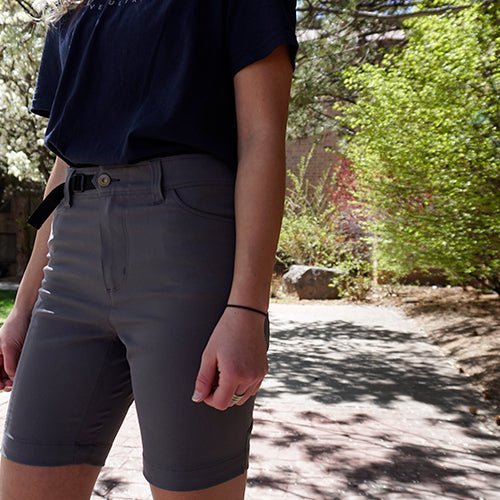 Close-up front view of a woman wearing Outdoor Vitals Satu Adventure Shorts outdoors, highlighting the integrated belt system, button closure, and side pockets.