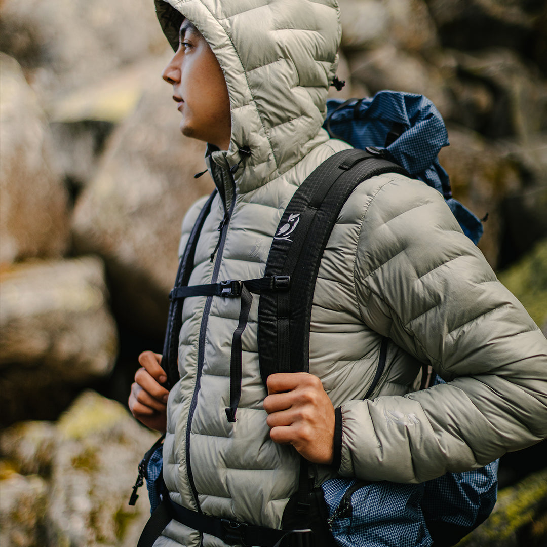 A hiker wearing a hooded NovaPro down jacket and a backpack in a rocky terrain.