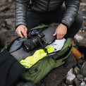 Top-down view of a person packing camera equipment, clothing, and gear inside the main compartment of the Outdoor Vitals KotaUL Ultralight Travel & Adventure Backpack while outdoors.